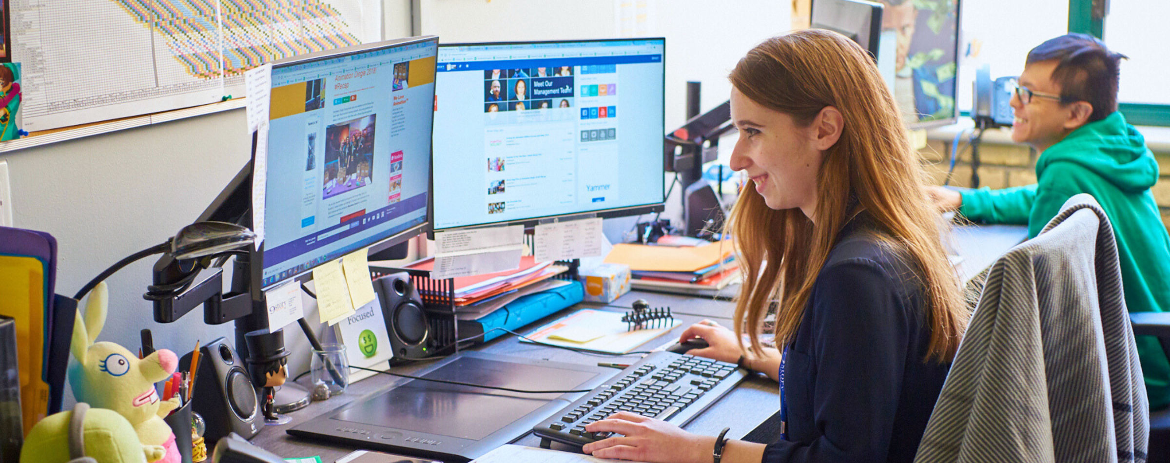 Two people sitting at their desks with computers and animation software open.