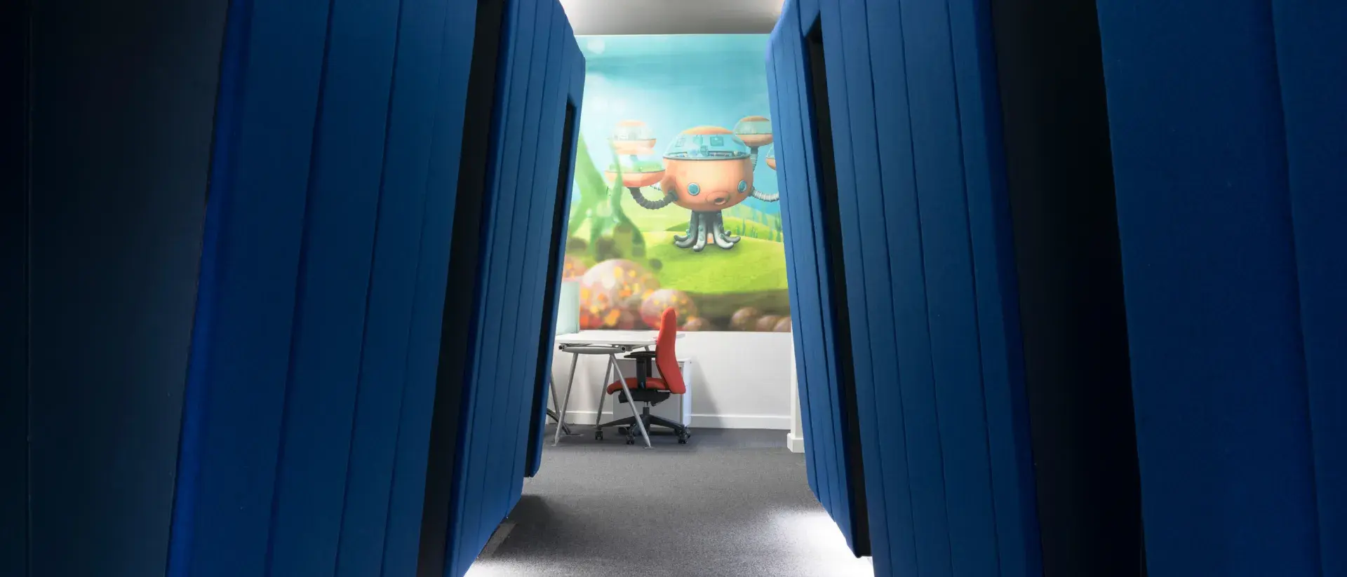 View through a blue corridor into a room with vibrant wall art.