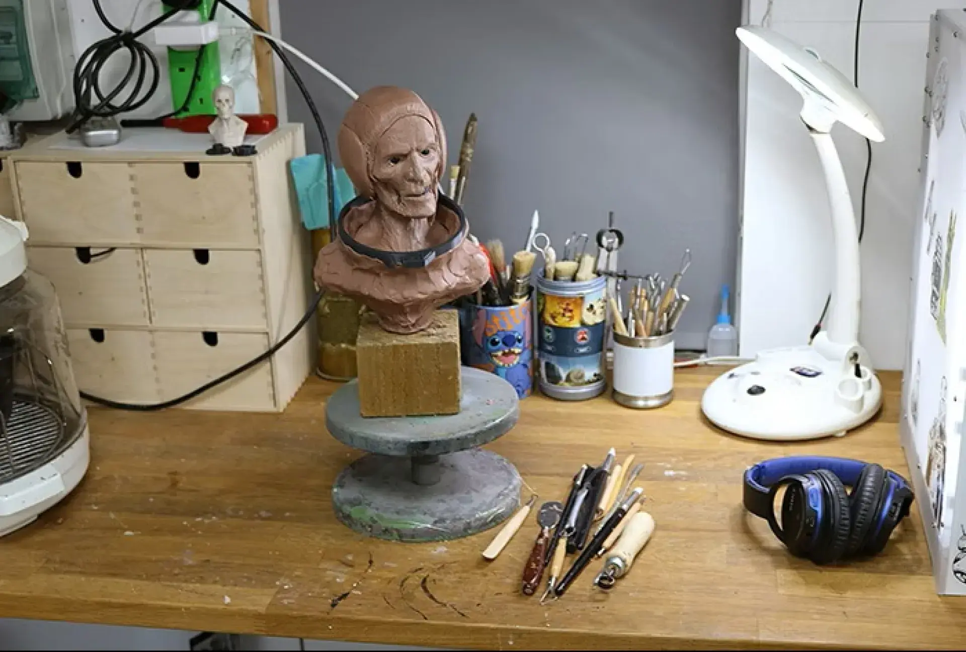 Sculpting workstation with clay bust on a turntable and tools organized nearby.