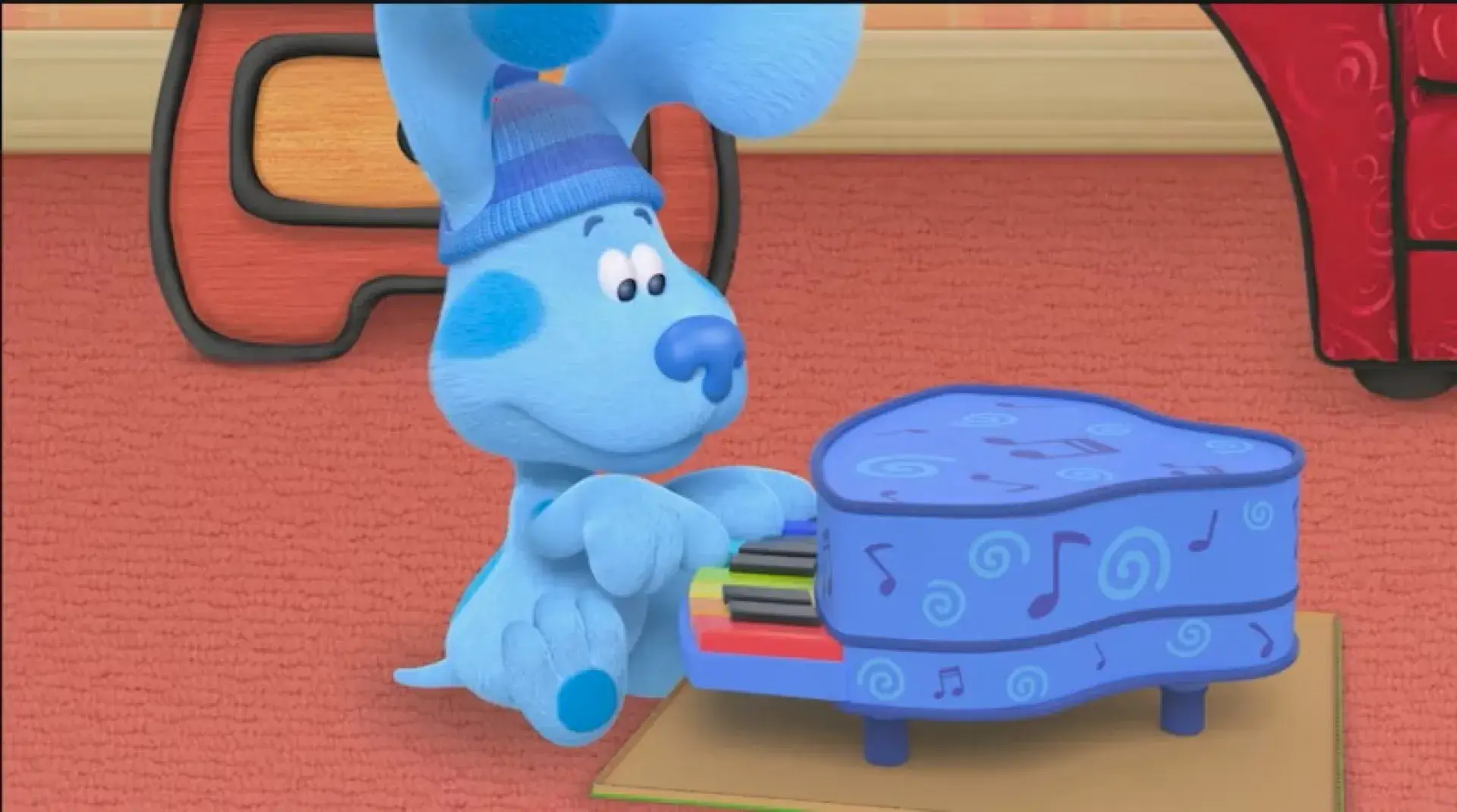 Blue playing a small blue piano with colorful keys while wearing a winter hat.