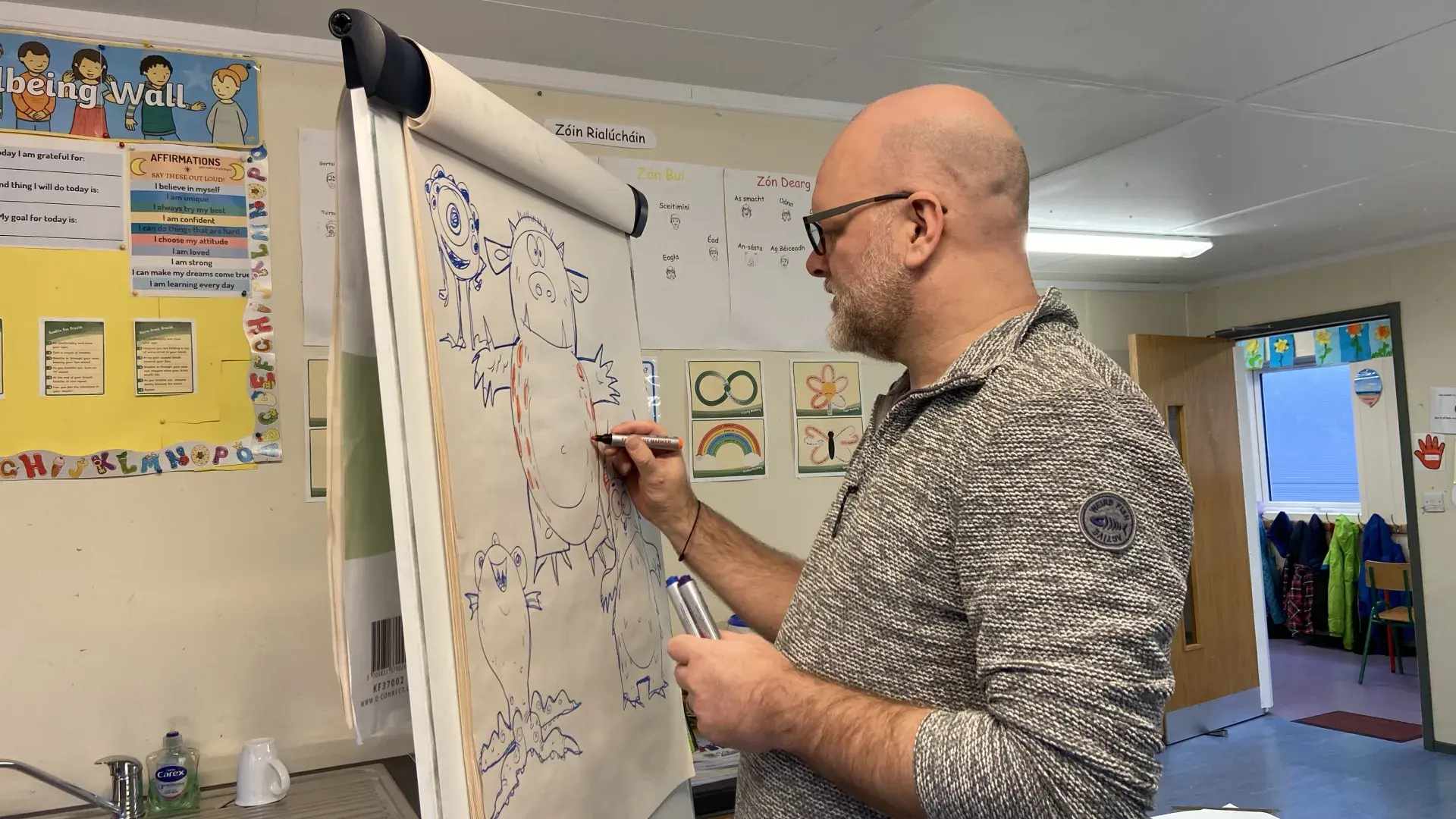 Person sketching cartoon characters on a flip chart in a classroom setting.