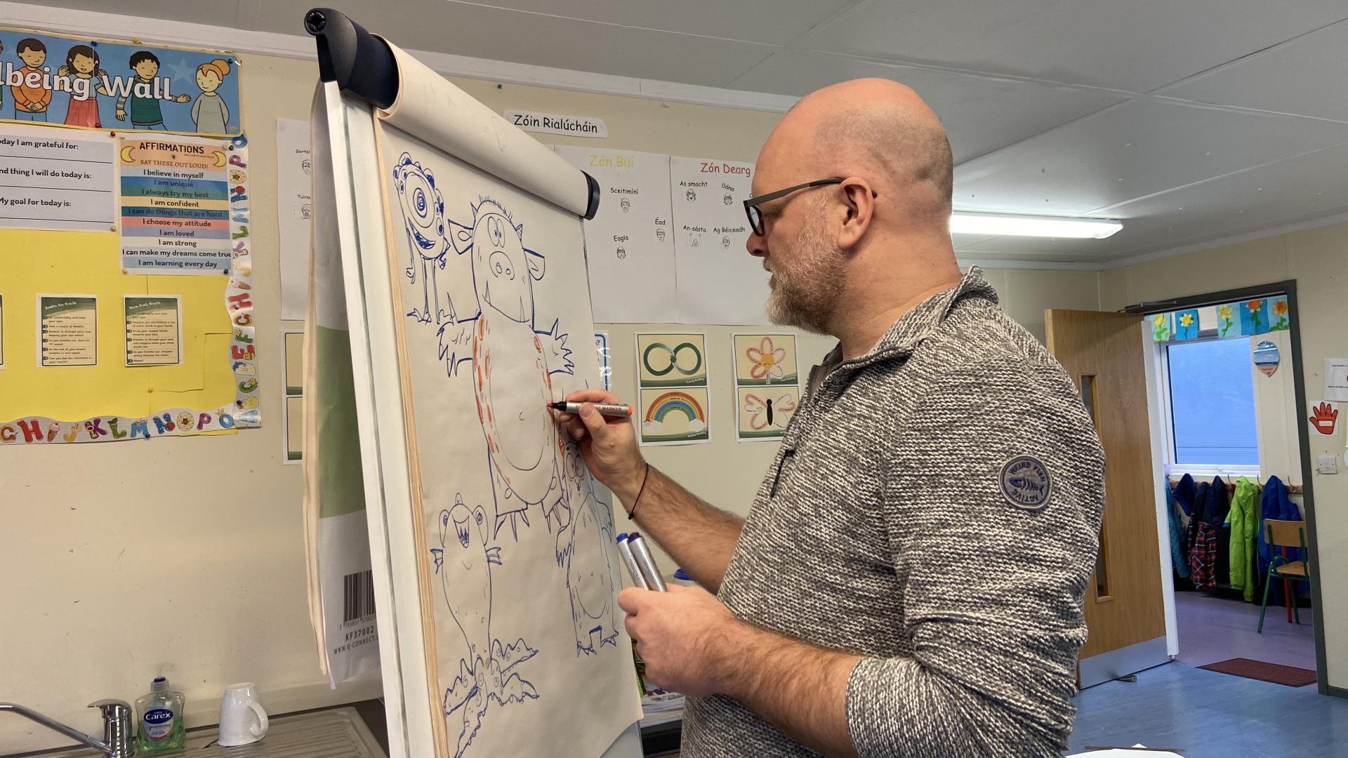 Person sketching cartoon characters on a flip chart in a classroom setting.