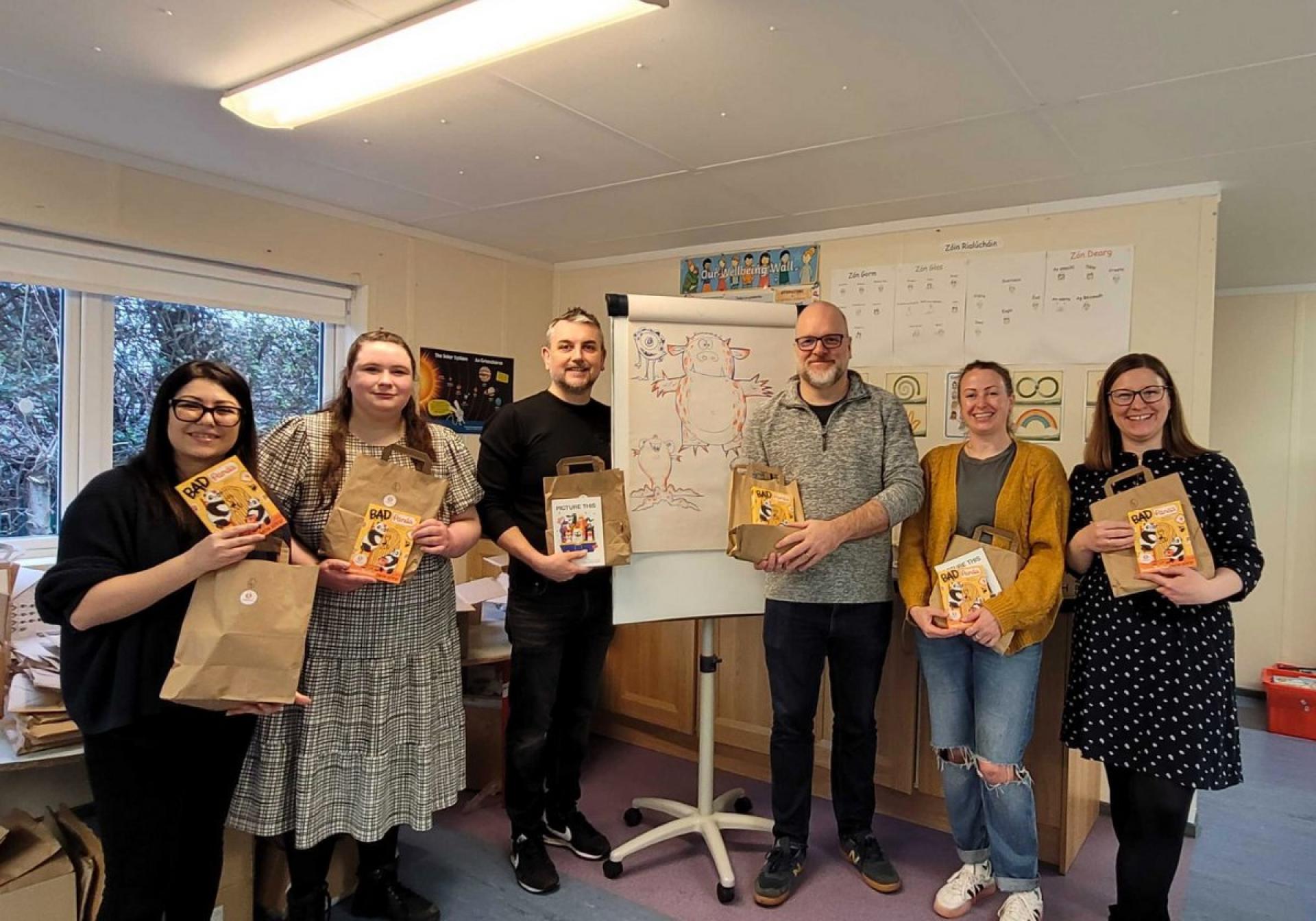 Group holding Bookbag packages and books in front of a flip chart with character drawings.