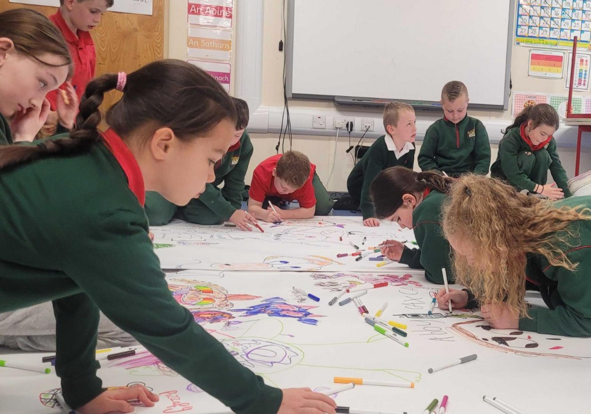 Children gathered around a large sheet drawing colorful characters with markers.