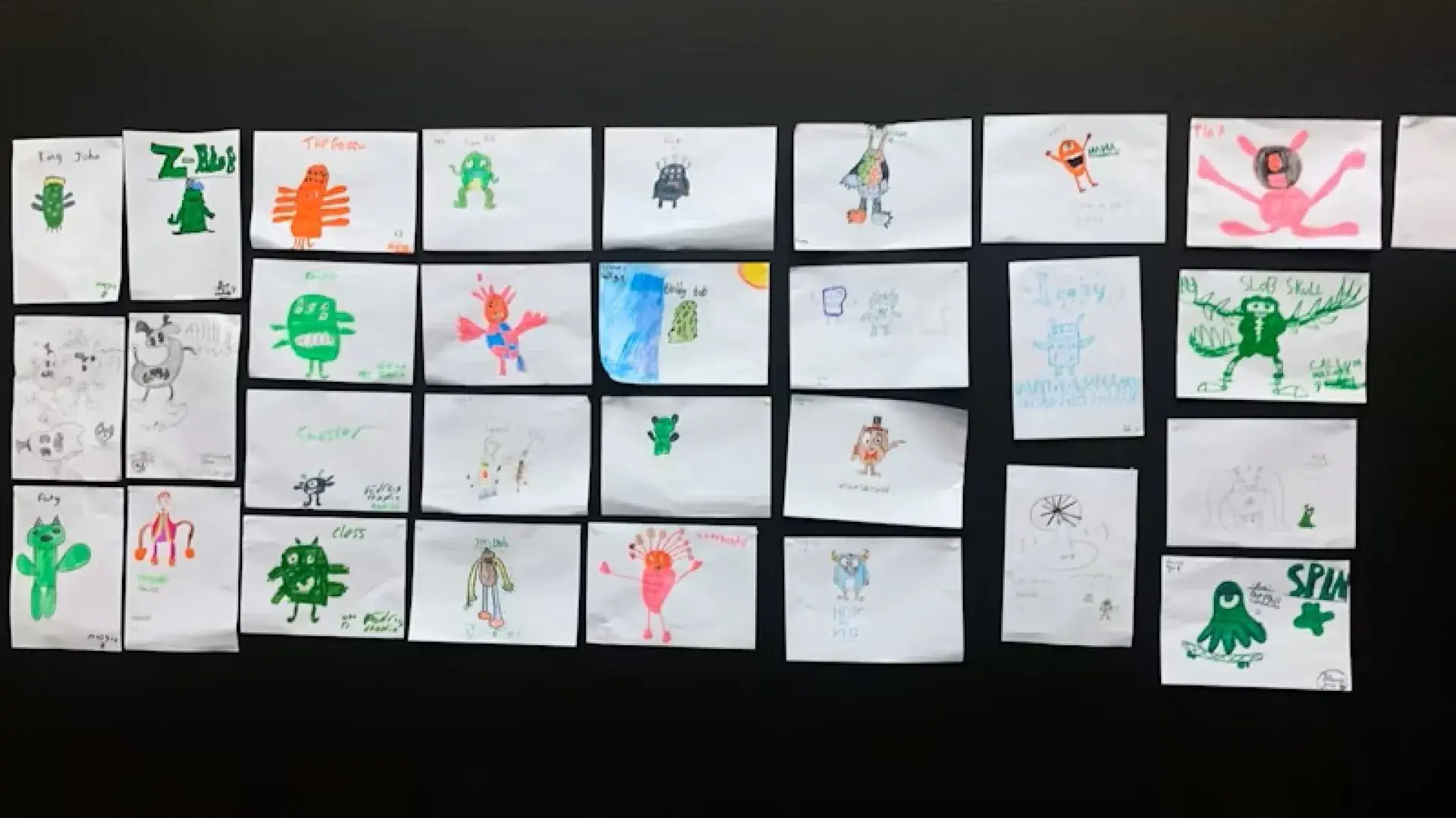 Wall display of multiple children’s monster drawings arranged in rows.