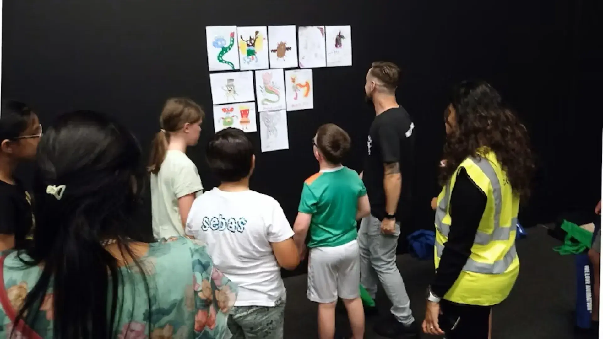 Group of children and adults viewing a wall display of monster drawings at the Community Games event.