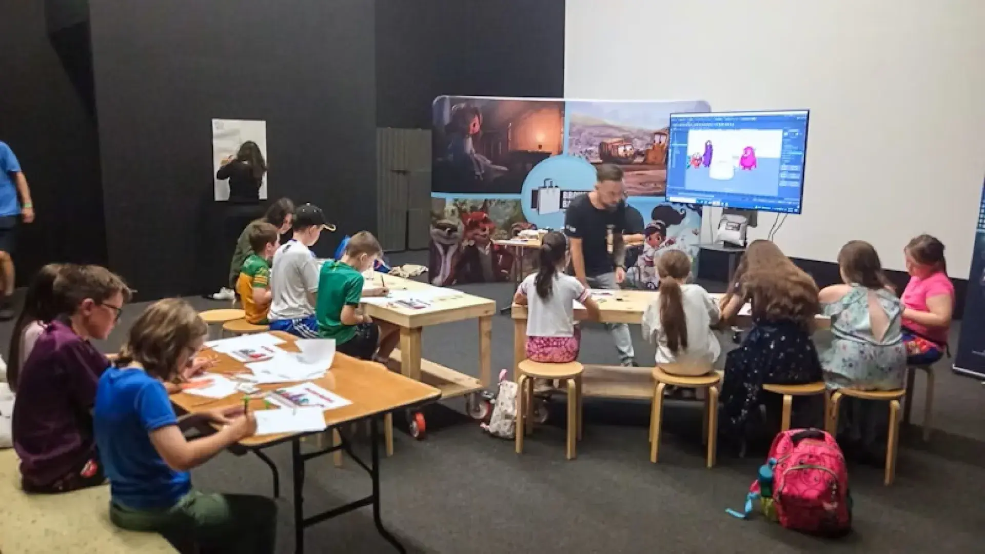 Children seated at tables during an animation workshop, drawing and coloring monster designs.