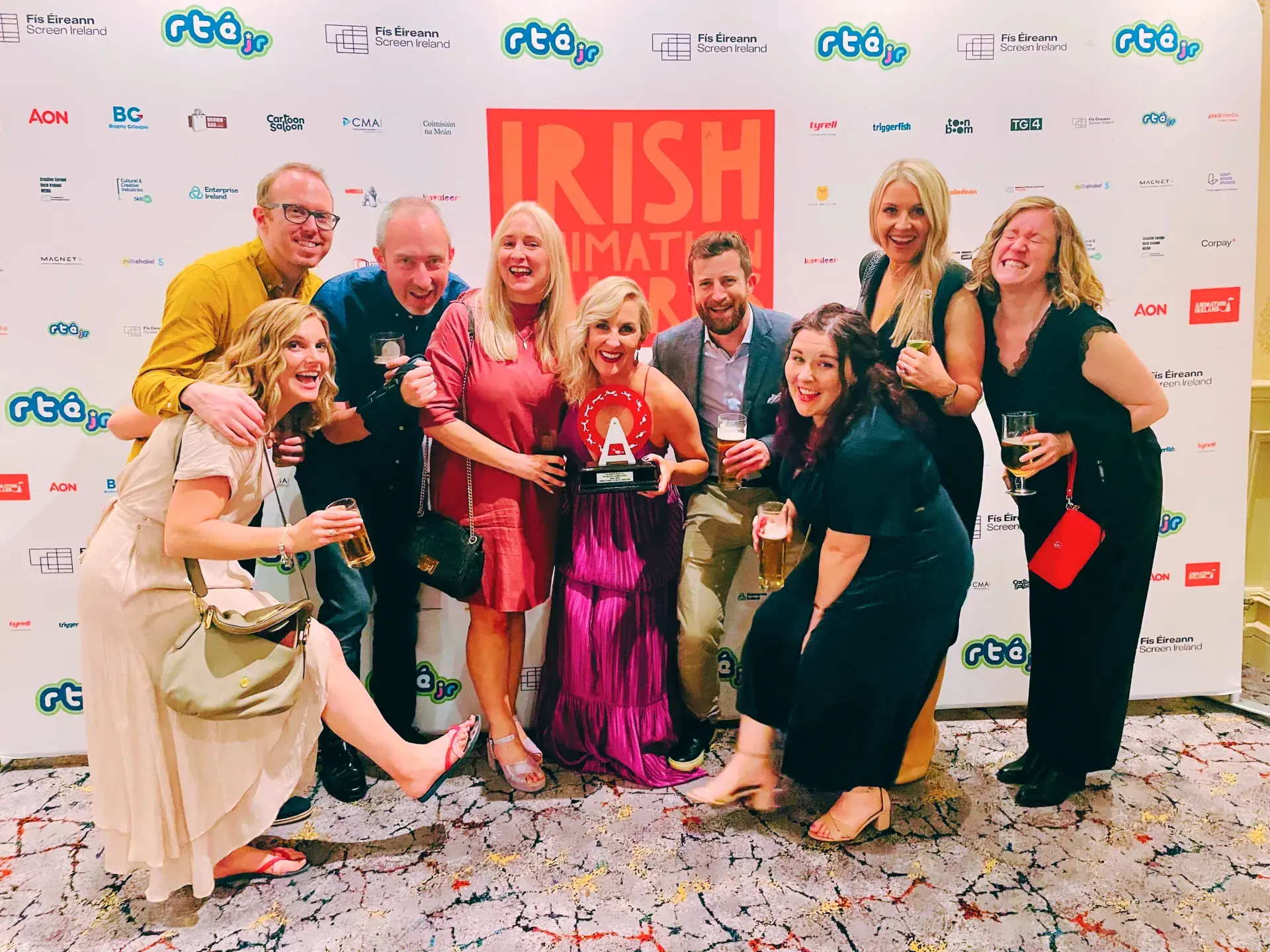 Large group posing in front of Irish Animation Awards backdrop with trophy held in center.