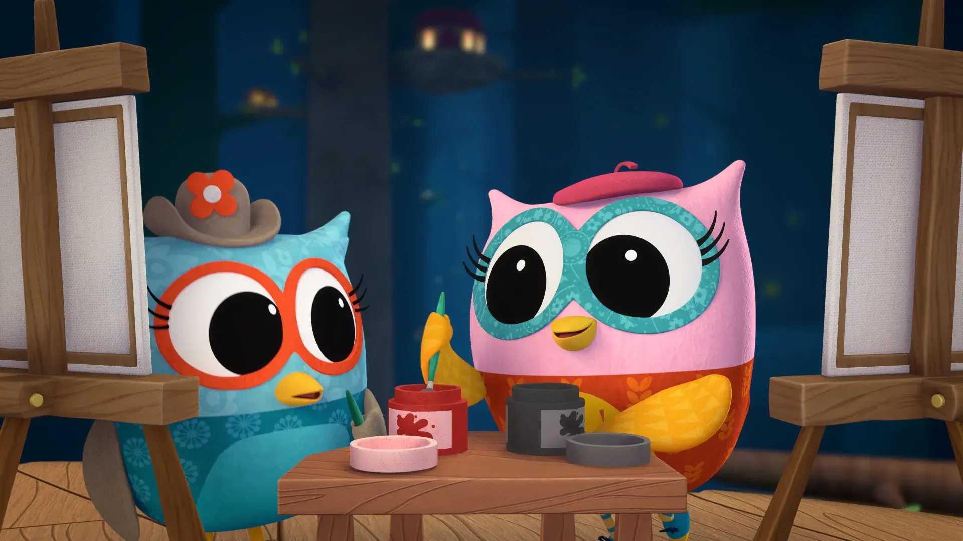 Two owl characters painting at easels with jars of colorful paint on a table in a nighttime forest setting.