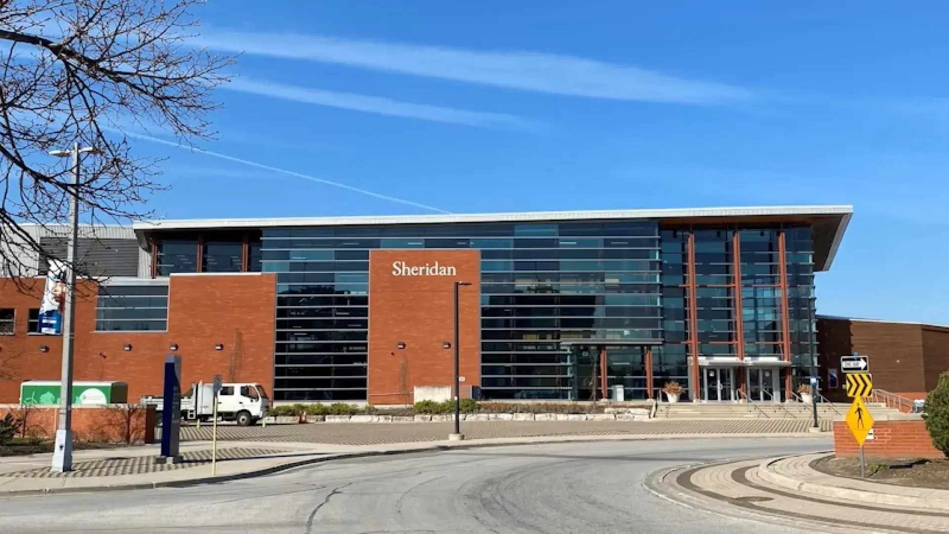 Exterior view of Sheridan College building with large glass windows and red brick facade under a clear blue sky.