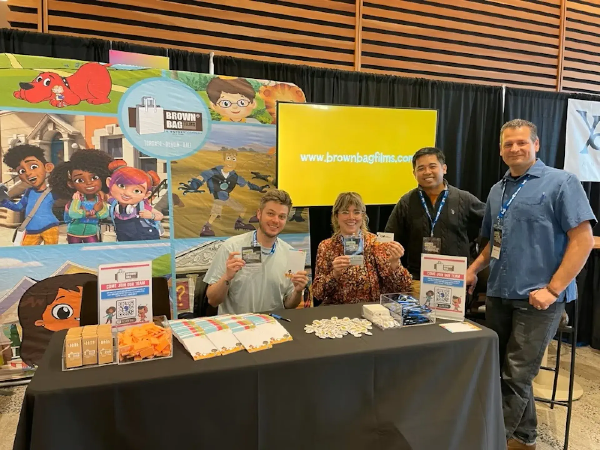 Brown Bag Films booth display featuring colorful character banners, branded signage, and giveaway items on the table.