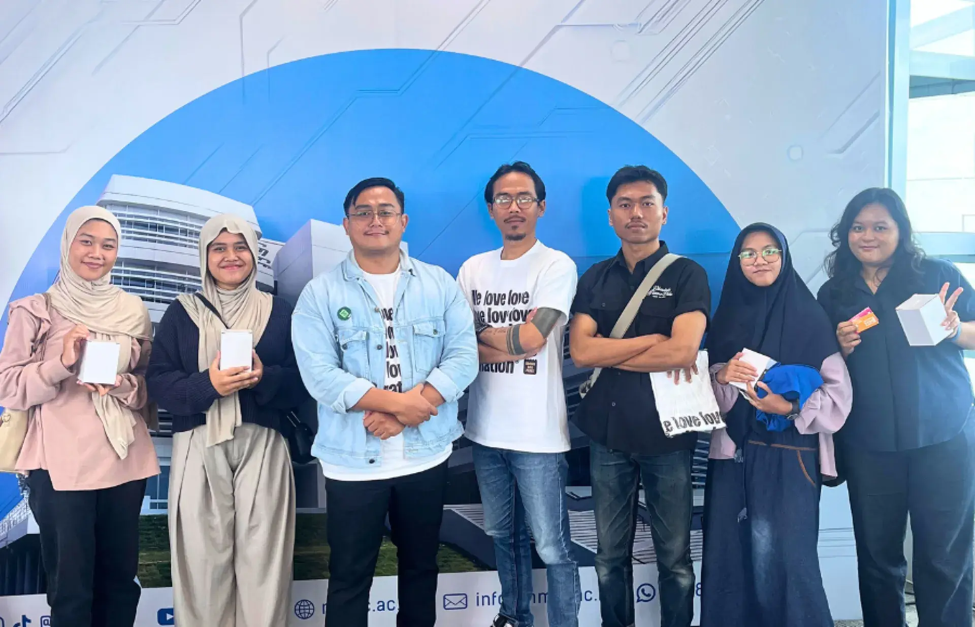 Group of participants holding boxed items, standing in front of a blue backdrop with building graphics.
