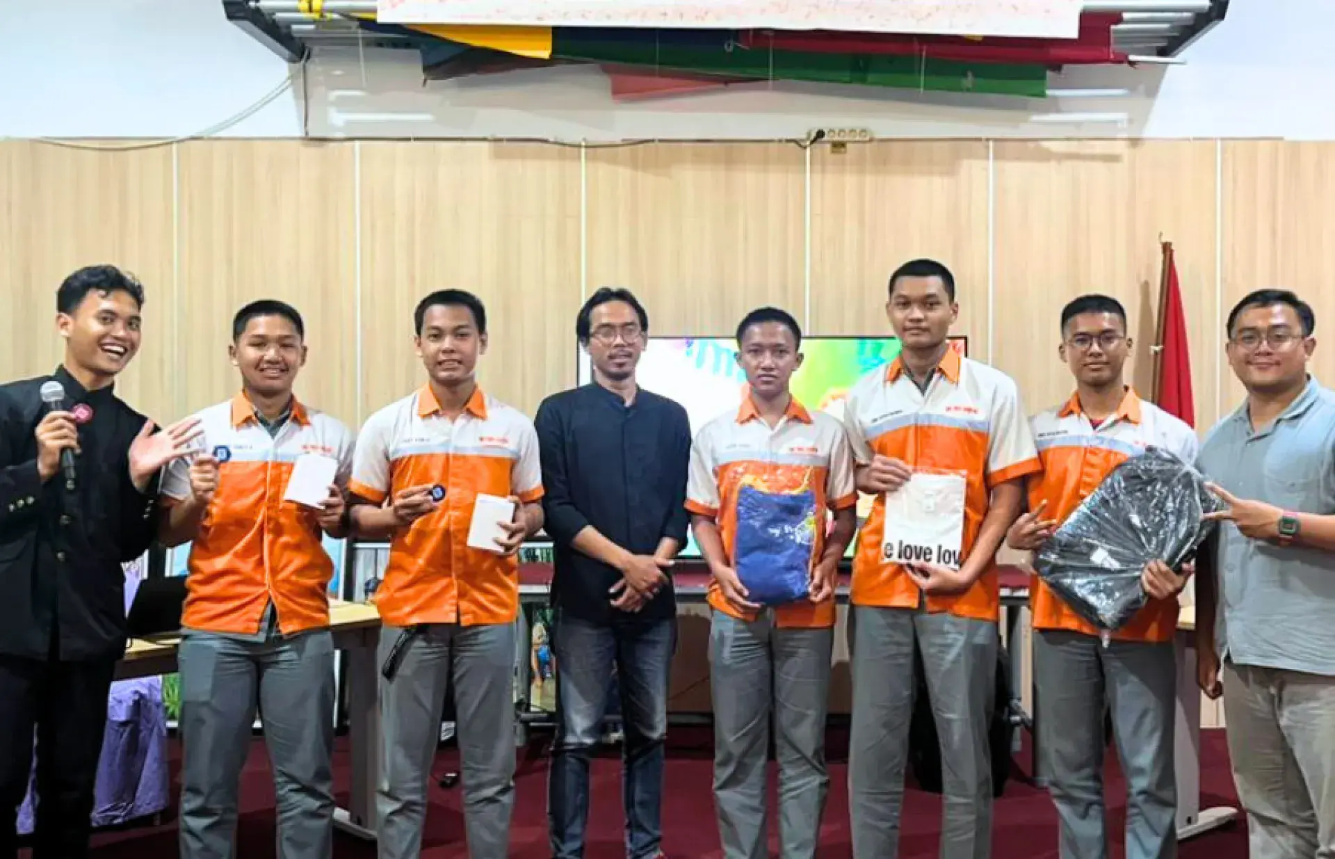 Line of participants in matching orange uniforms holding gifts or boxes during a presentation event.