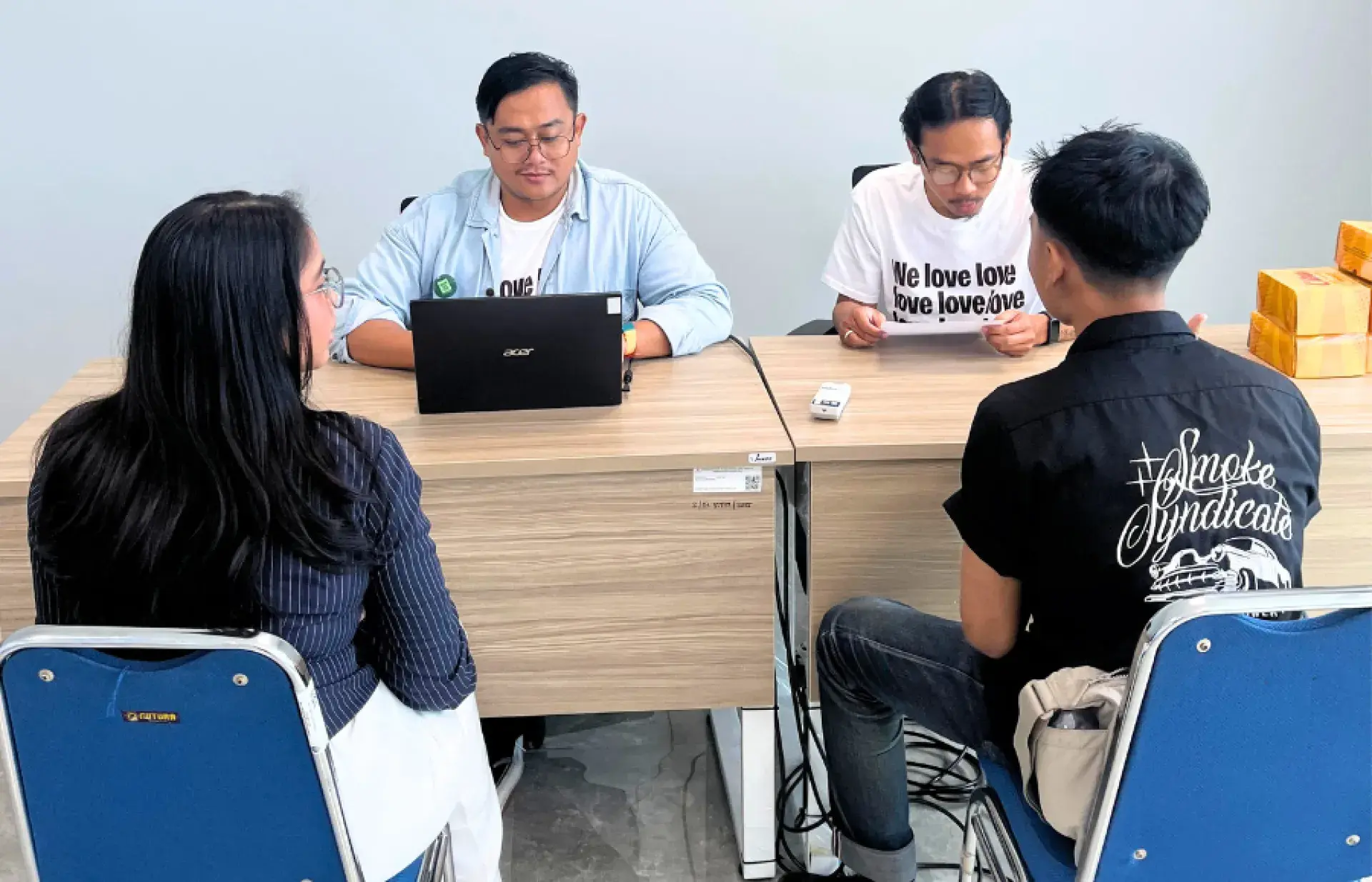 Two people seated behind tables facing two students in a simple office setting.