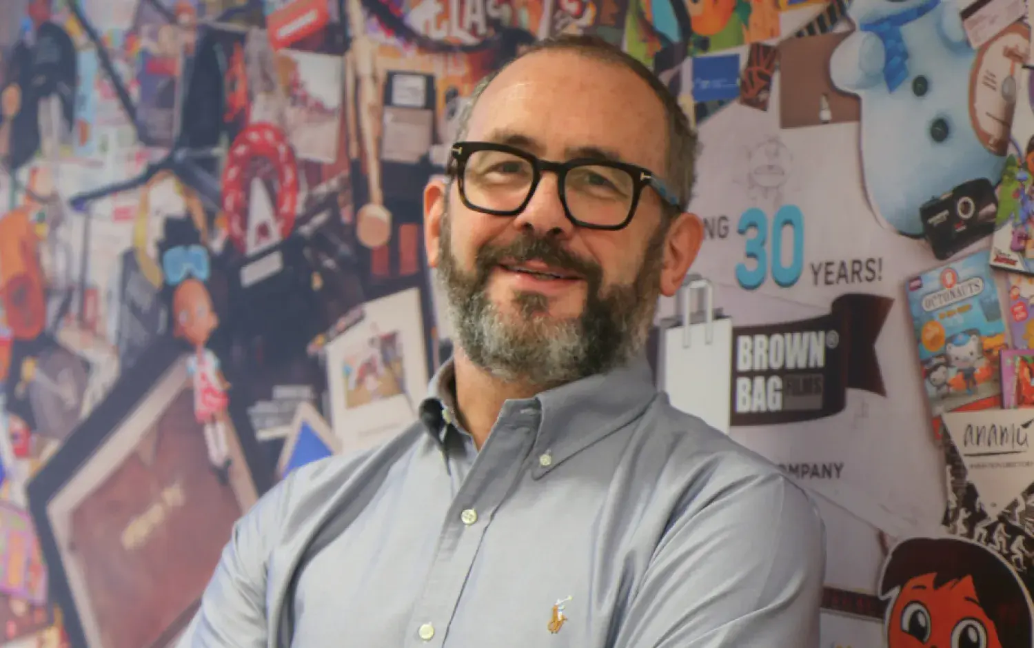 A photo of Cathal Gaffney, a colourful wall featuring a collage of Brown Bag Films' history behind him.