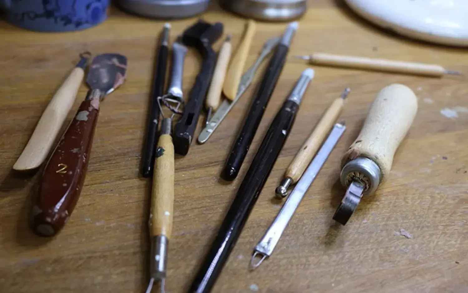 Assorted sculpting tools laid out on a wooden workbench for clay detailing.