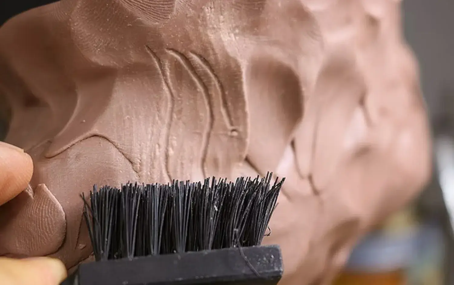 Close-up of a sculpting brush smoothing textured clay surface.