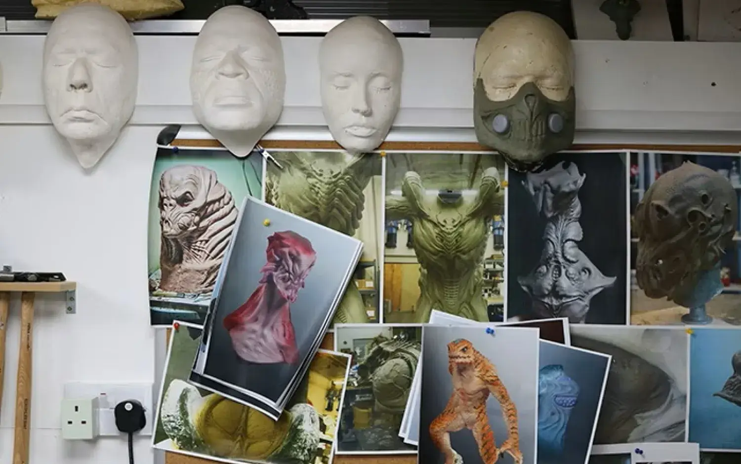 Wall display of creature design references and sculpted masks in a studio.