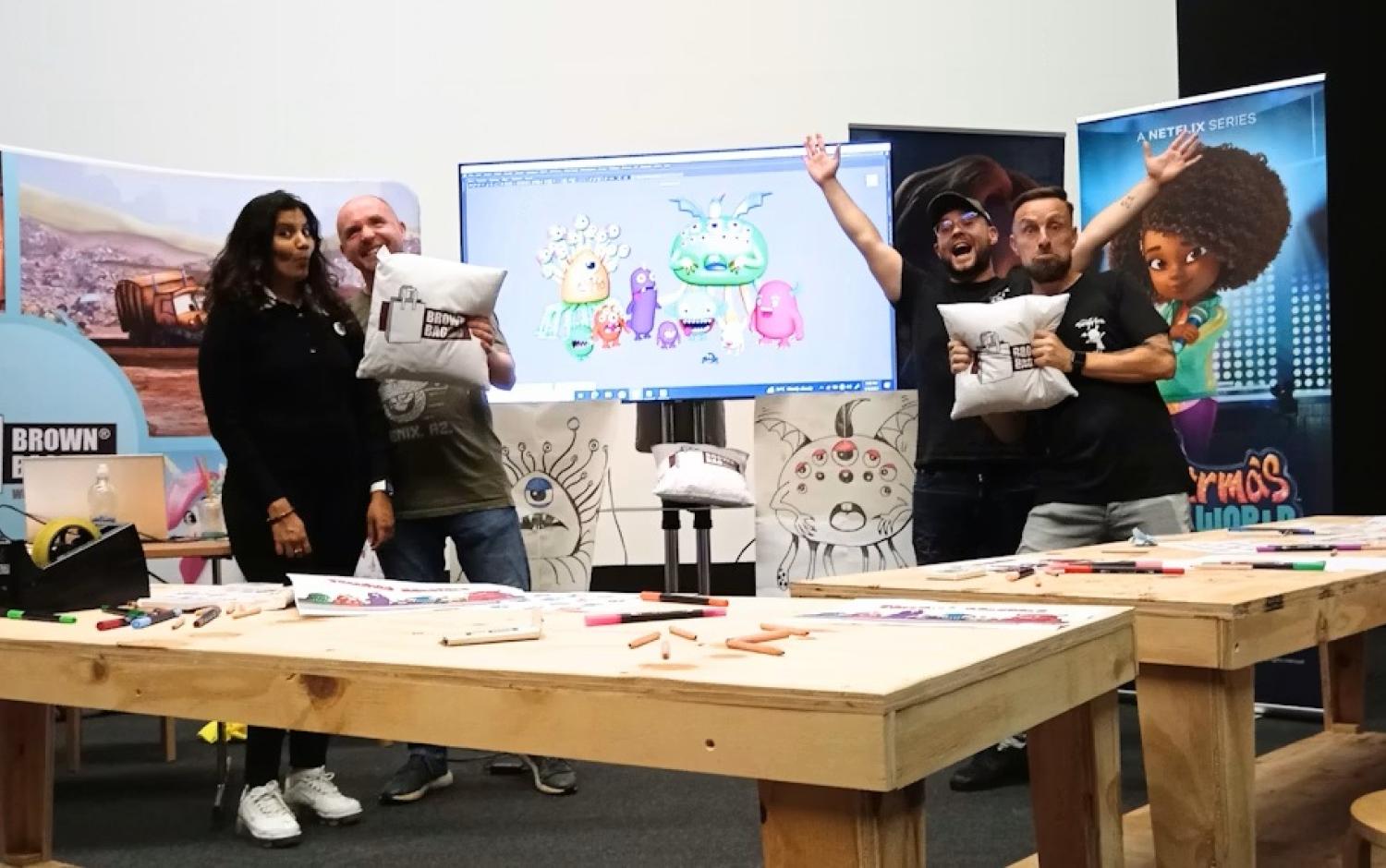 Workshop setting with tables, art supplies, and Brown Bag Films staff members holding pillows featuring Brown Bag Films' logo.