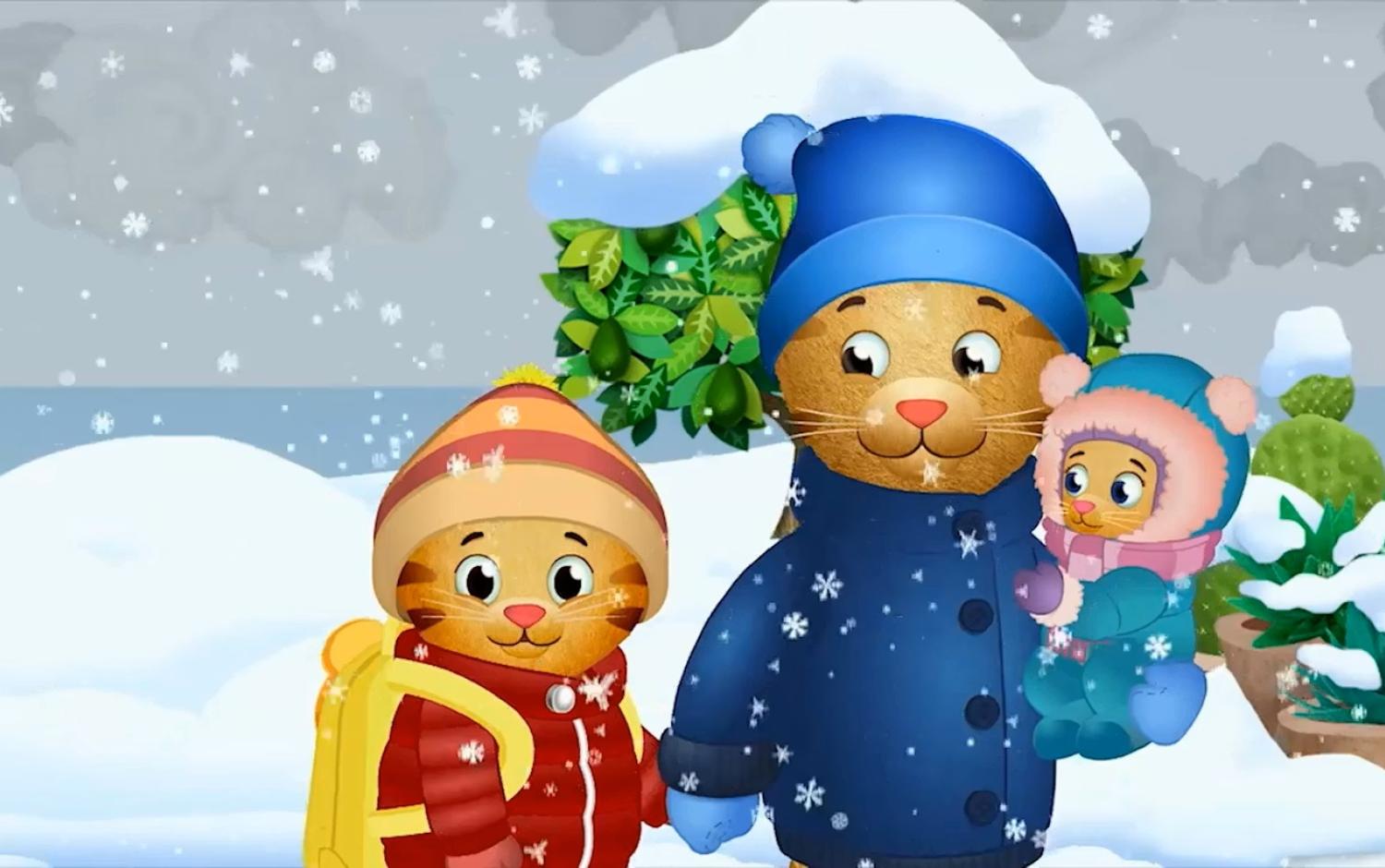 Daniel Tiger and family dressed in winter coats and hats, standing in a snowy outdoor scene with falling snowflakes and green shrubs in the background.