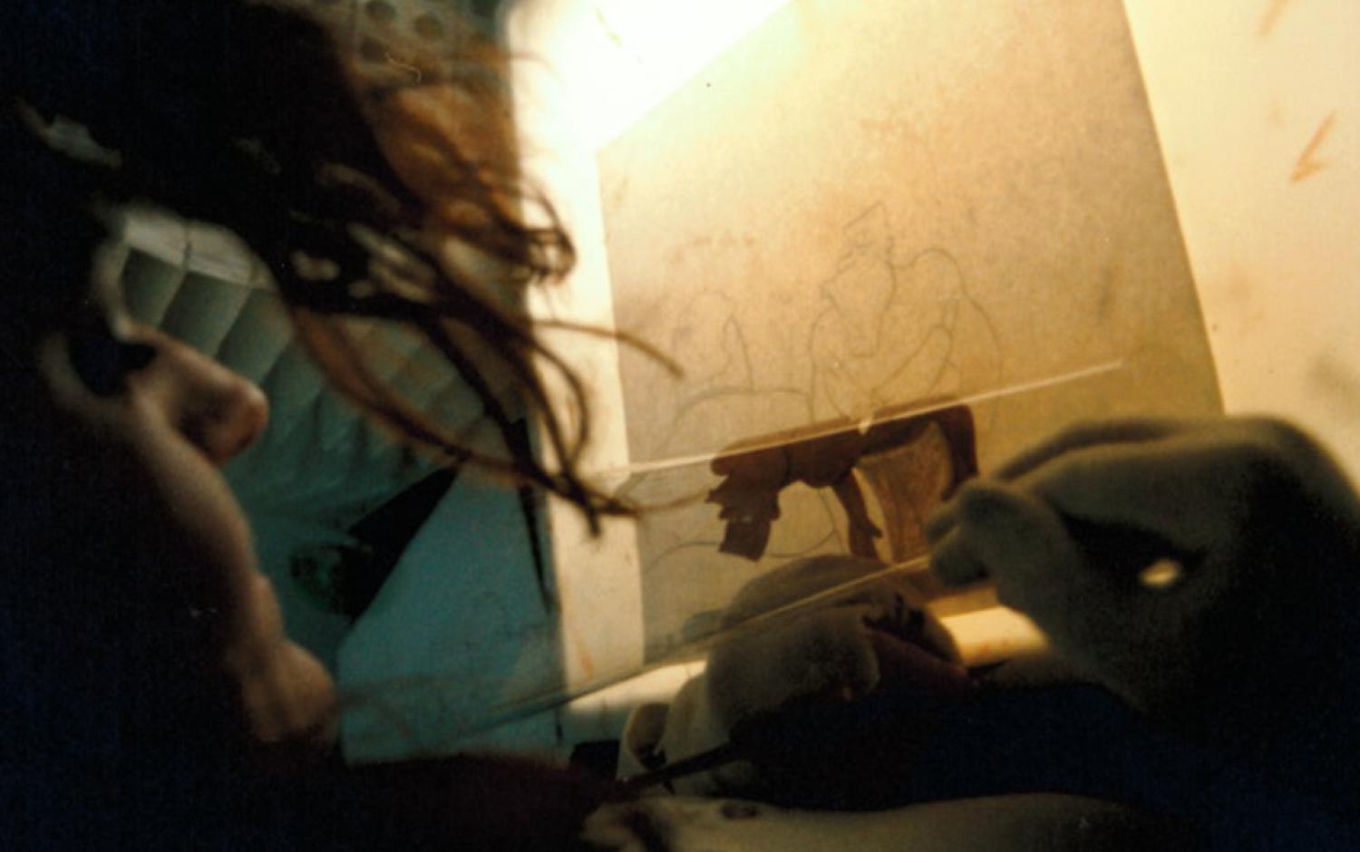 Close-up of animation cel painting on a lightbox, showing a character sketch being filled with color.