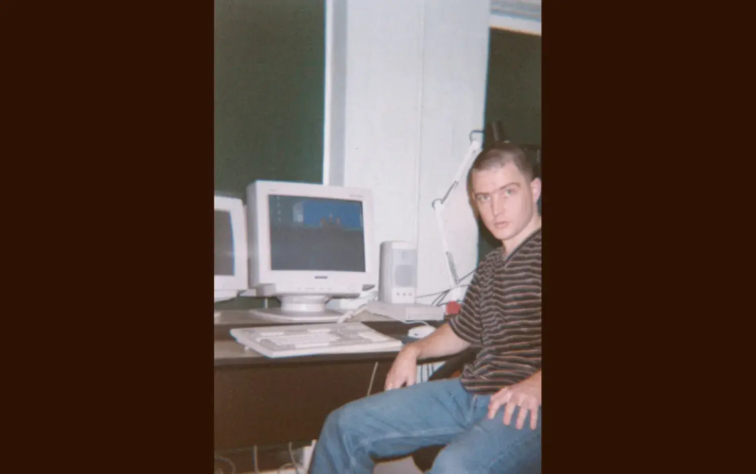 Person seated at a desk with two CRT monitors and a keyboard, working in a computer setup.