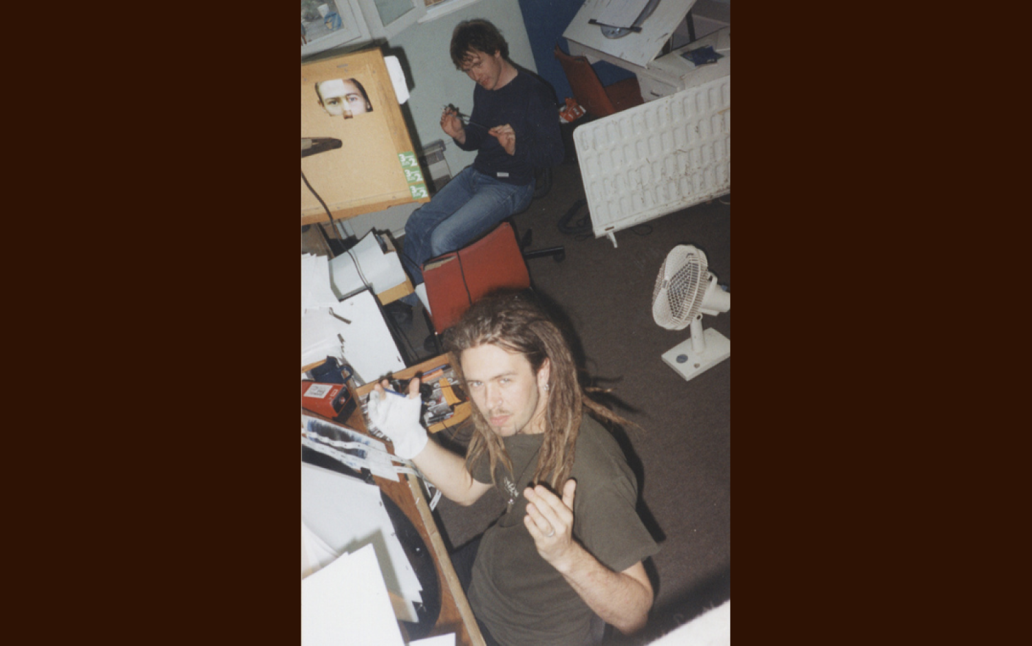 Overhead view of two people at animation desks in a studio, one holding a pencil and paper, the other working near a fan.