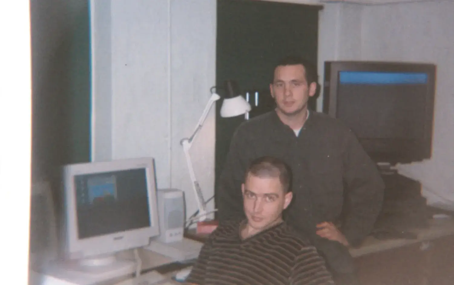 Two people in a studio with a computer and a TV screen displaying colorful animation.