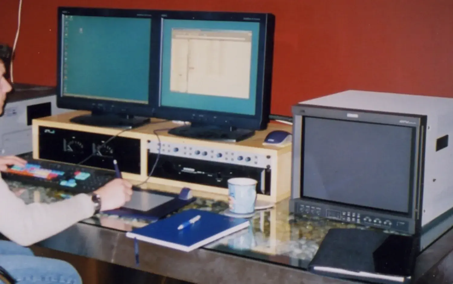 Person working at a desk with two computer monitors, audio equipment, and a graphics tablet.