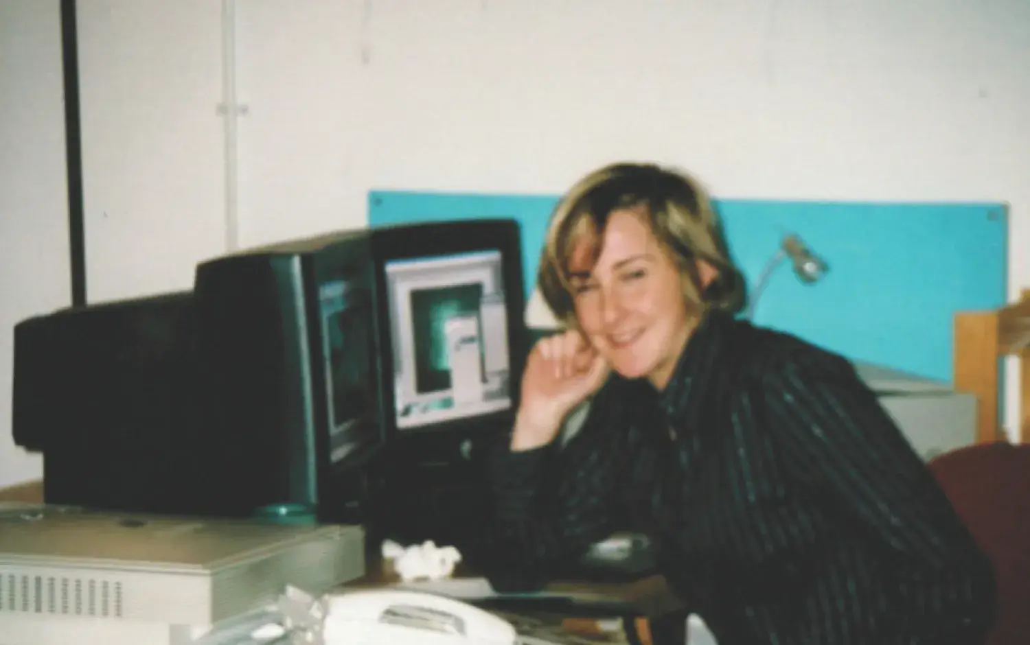 Person seated at a desk using a computer with a CRT monitor displaying a design or animation interface.