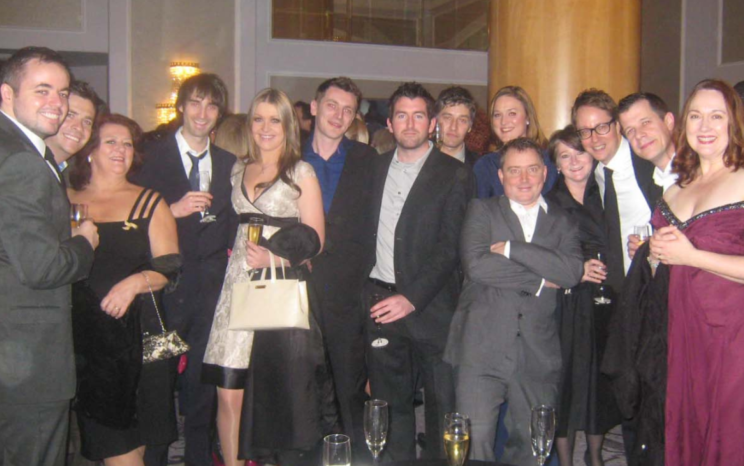 Large group of people in formal attire gathered at a reception, holding champagne glasses.