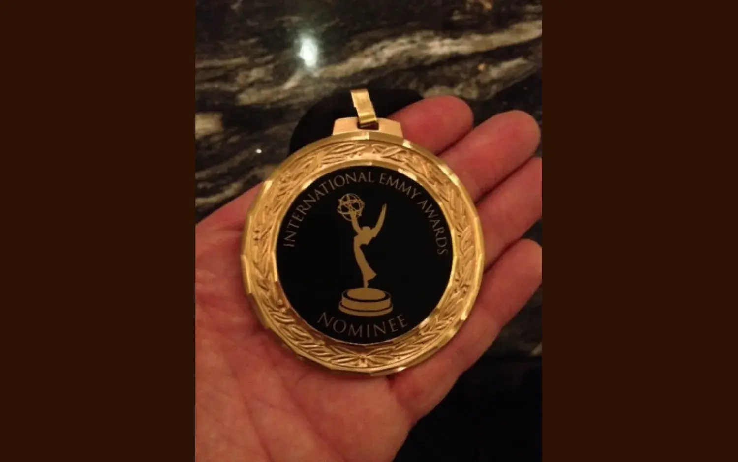 Close-up of a gold International Emmy Awards nominee medal resting in a hand.