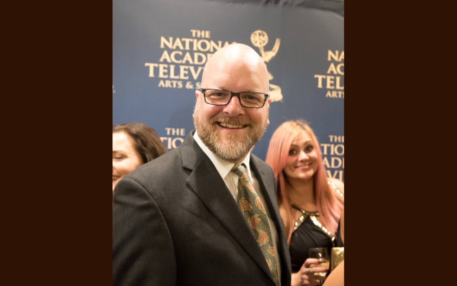 Person in formal attire standing in front of Emmy Awards backdrop.