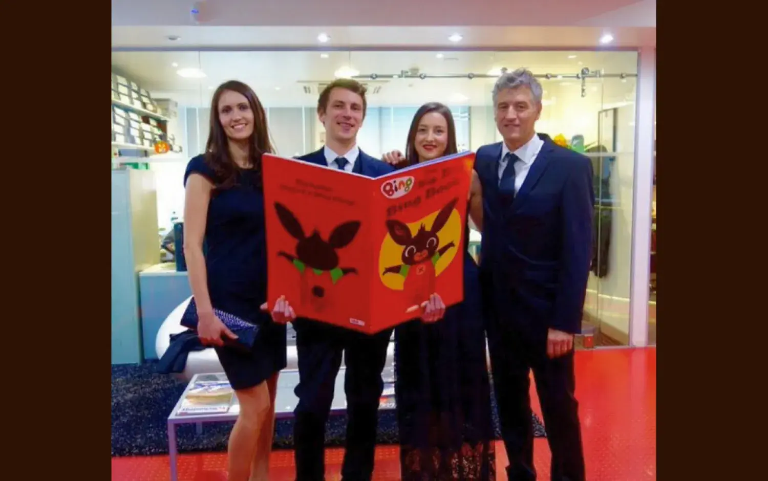 Four people holding a large illustrated Bing book in a brightly lit room.