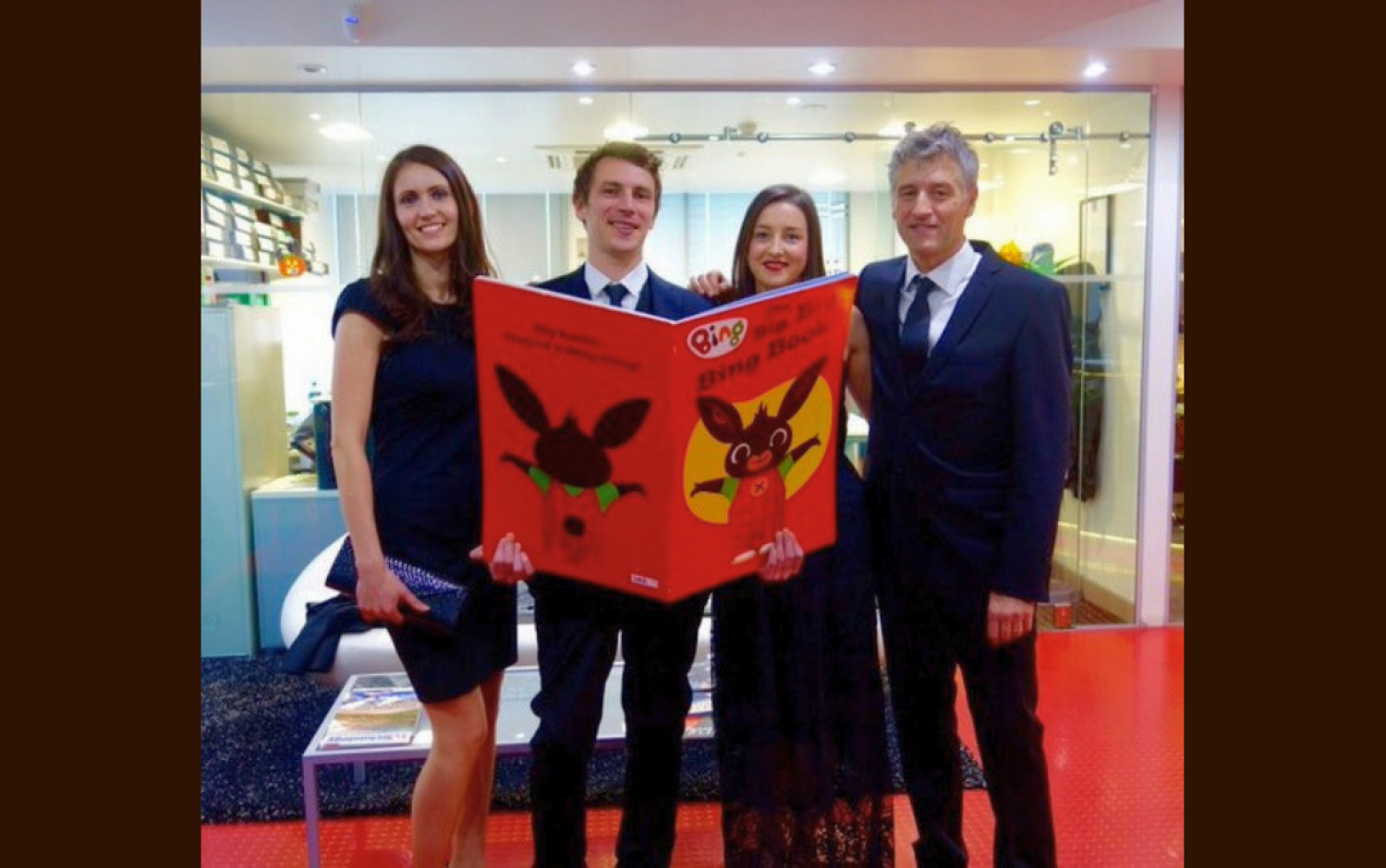 Four people holding a large illustrated Bing book in a brightly lit room.