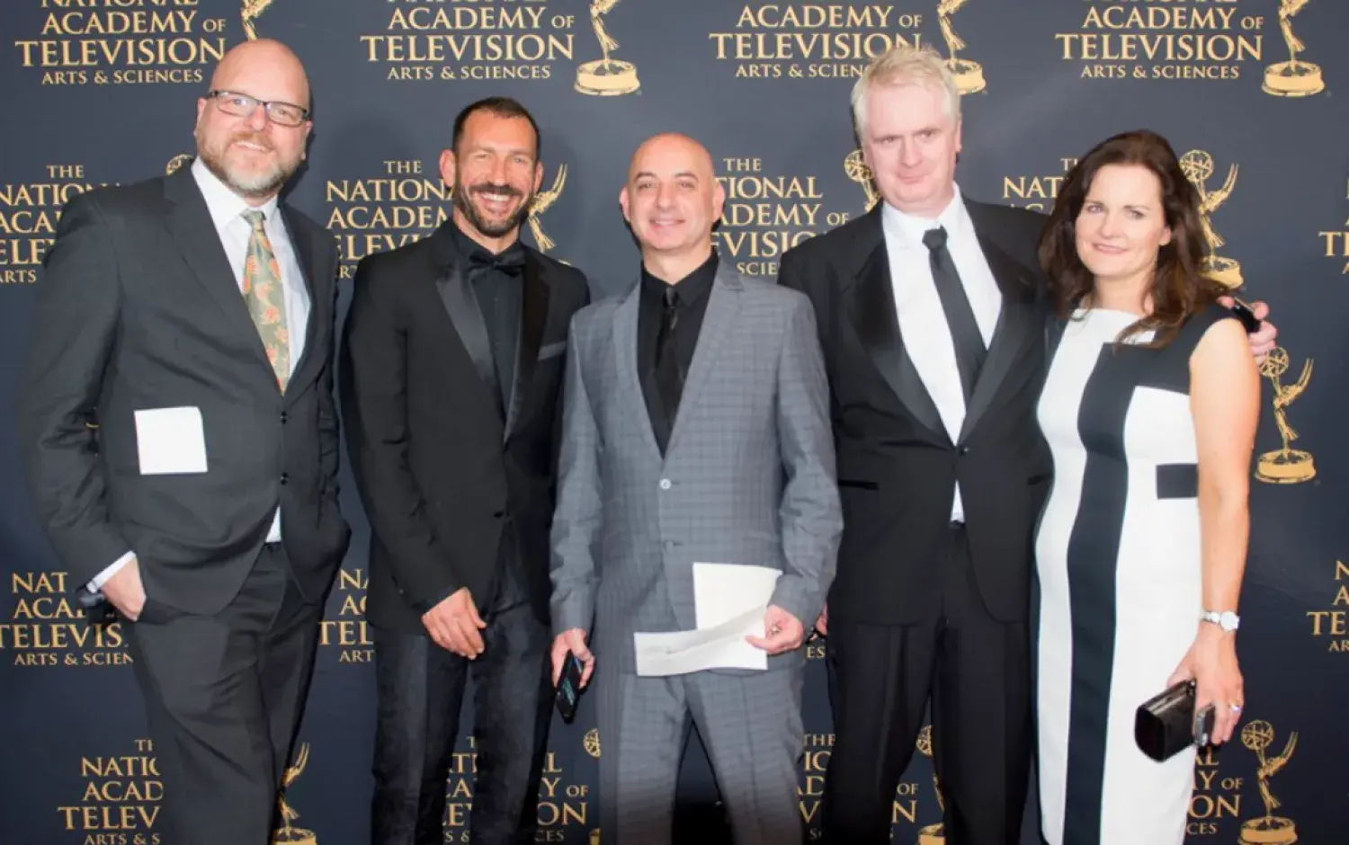 Group of five people posing on Emmy Awards red carpet in formal attire.