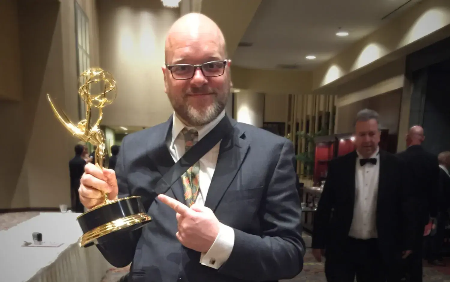 Person in a suit holding an Emmy Award trophy at a formal event.