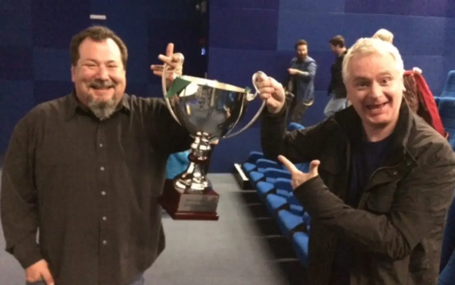 Two people standing in a theater holding a large silver trophy cup.