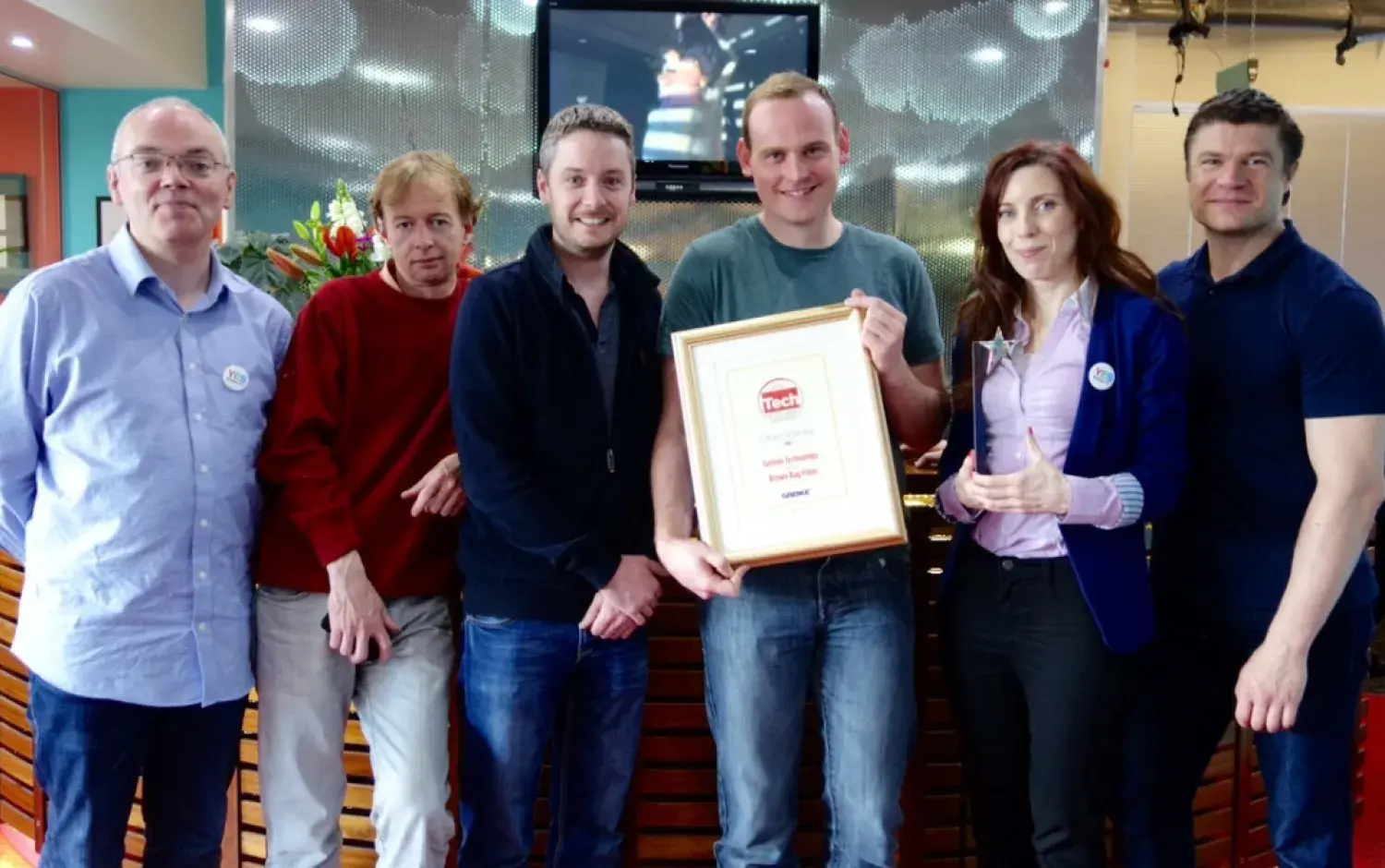 Six people standing indoors, holding a framed Tech Excellence Award certificate.