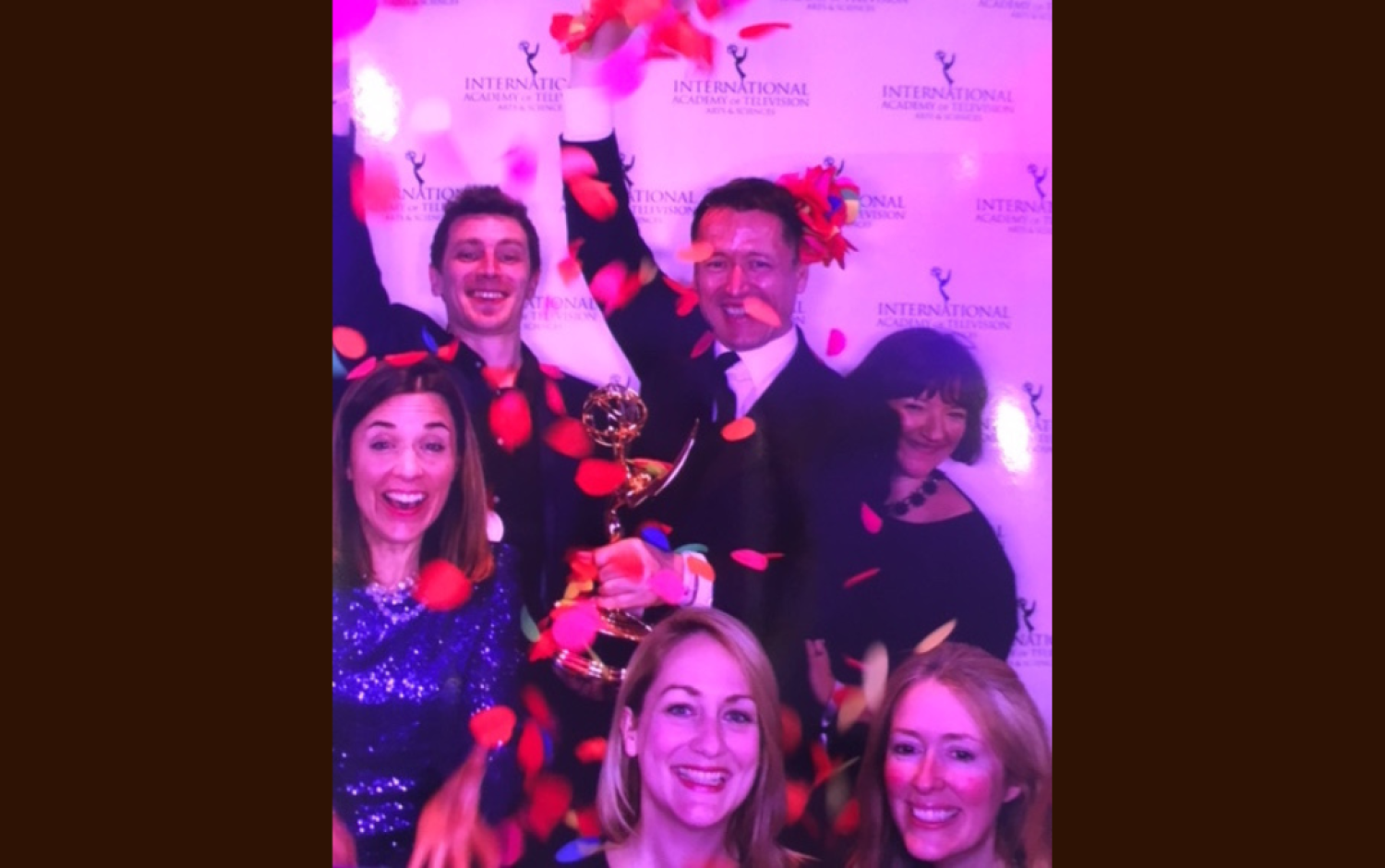 Celebratory photo with rose petals falling and an Emmy Award held high.