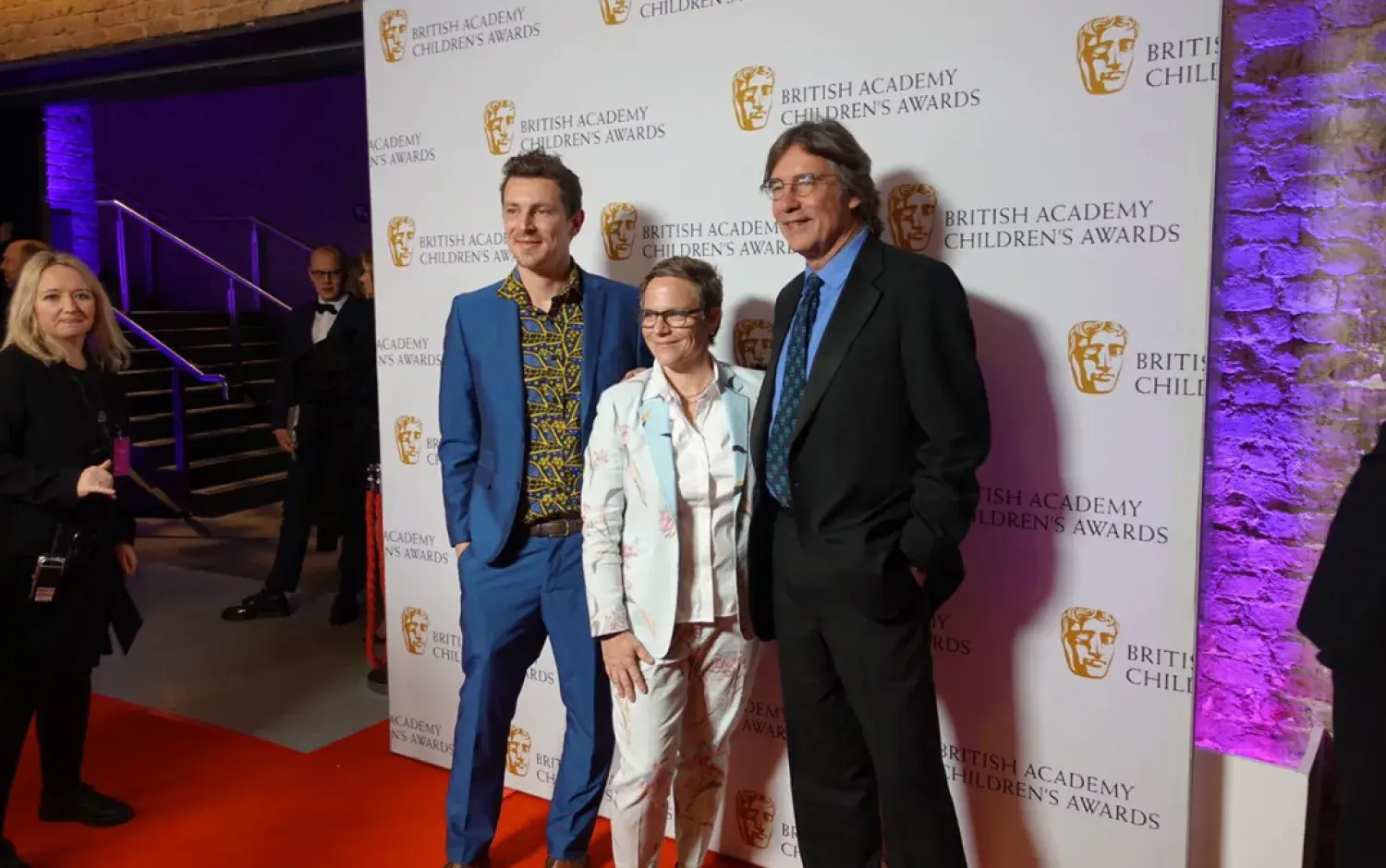Three people posing on the red carpet in front of a British Academy Children’s Awards backdrop.