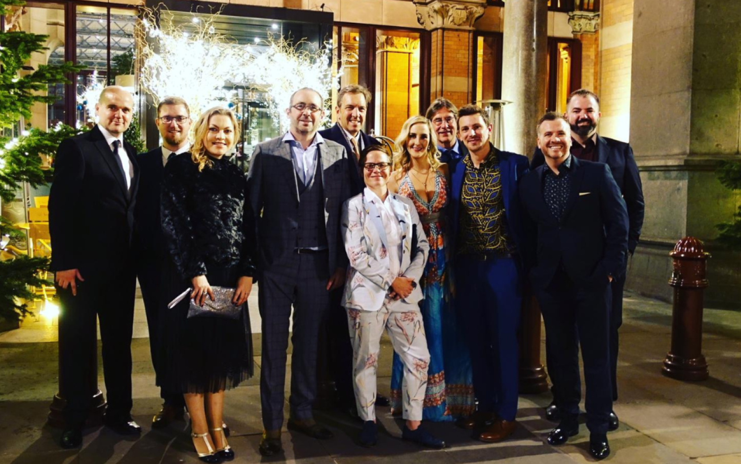 Group standing outside a building decorated with festive lights and greenery.