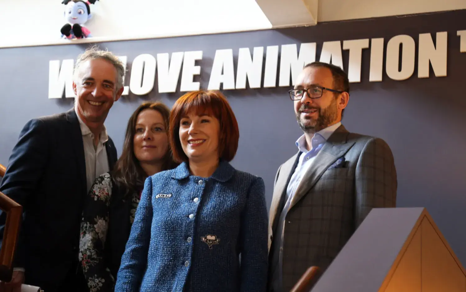 Group standing under a sign that reads “We Love Animation” inside an office space.