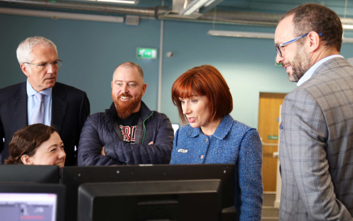 Individuals observing computer screens in an open-plan office environment.