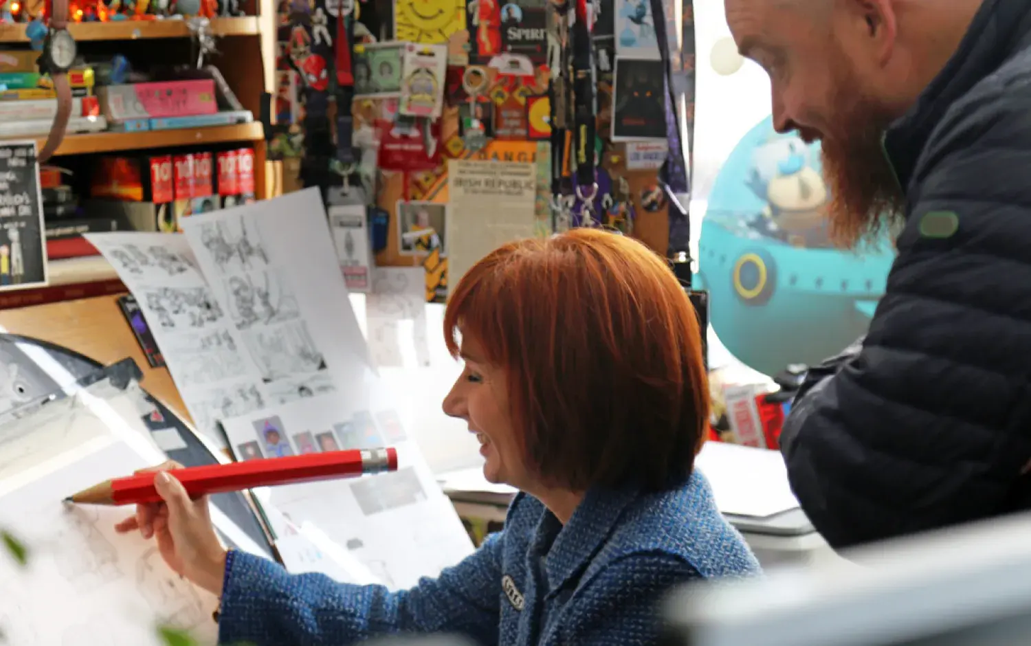 Person demonstrating drawing techniques at a cluttered desk filled with art supplies and sketches.