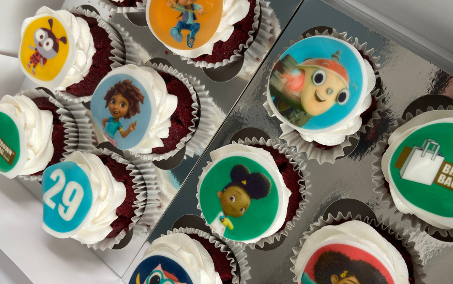 Box of cupcakes decorated with edible images of characters, logos, and the number 29.