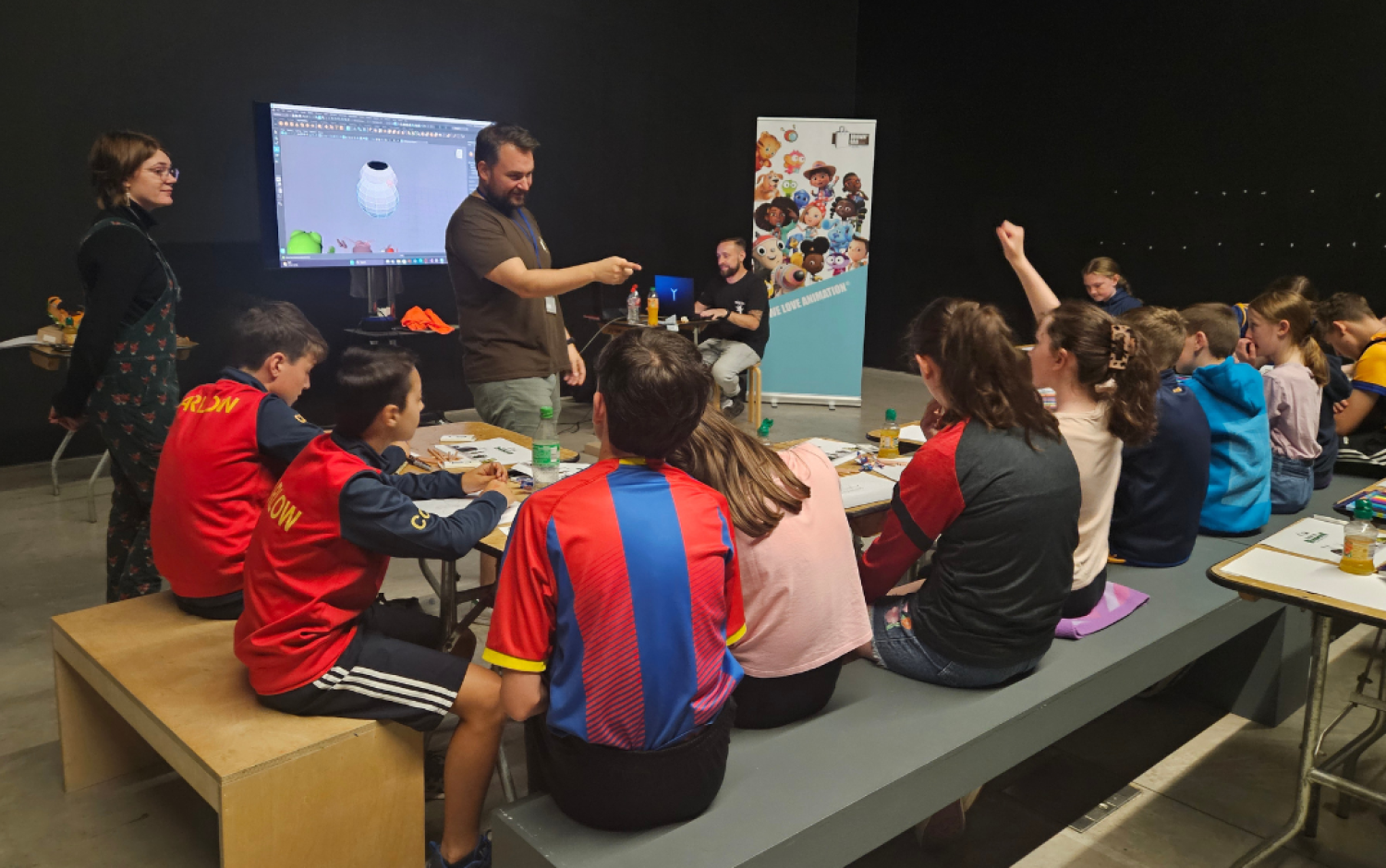 Children seated at tables participating in an animation workshop with a presenter and screen.
