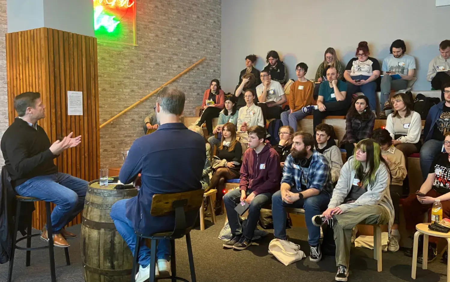 Audience seated in a casual venue listening to two speakers during a discussion session.