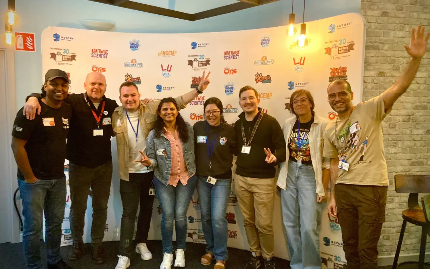 Group of eight people posing in front of a branded backdrop at an event.