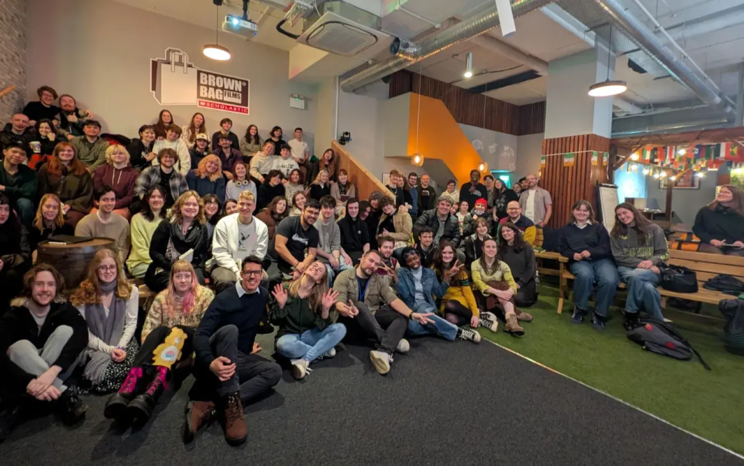 Wide group photo of people seated and standing in a modern office space during a company gathering.